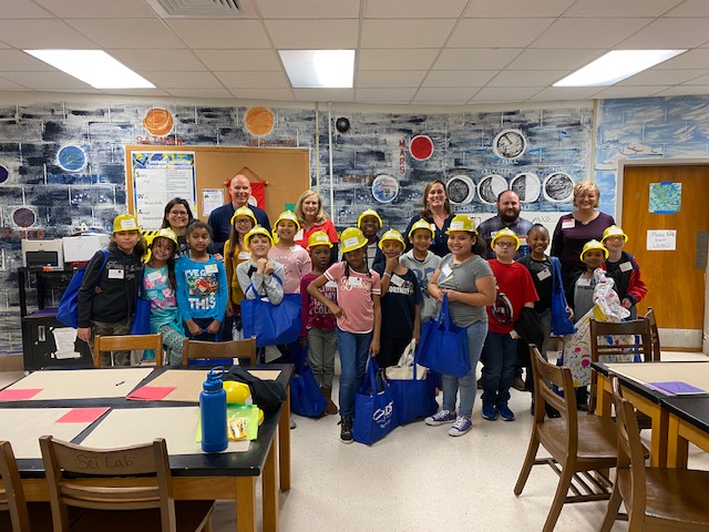 Cassie and the other three adult judges stand with the group of fourth grades who participated in the competition. The fourth graders are wearing kid’s construction hats.